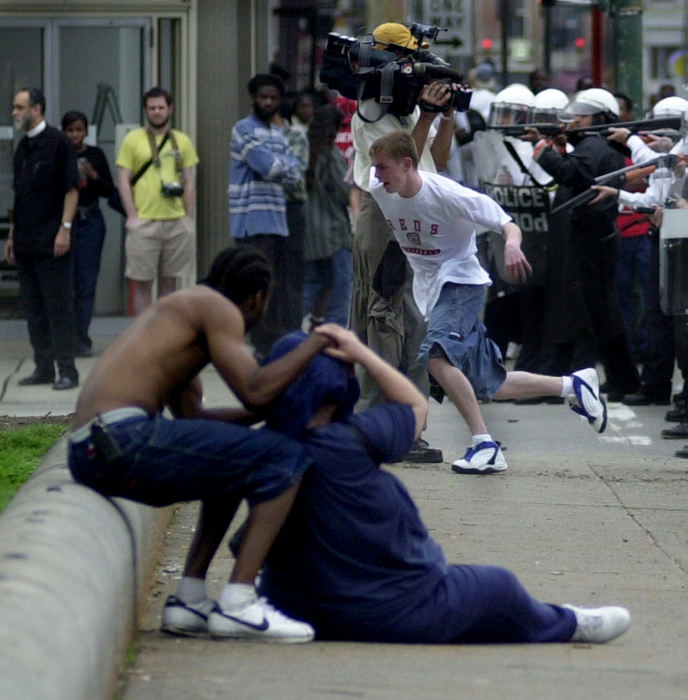 Award of Excellence, News Picture Story - Brandi Stafford / The Cincinnati EnquirerA young man runs from Cincinnati police officers as they shoot bean bags into a crowd, wounding one woman shown being helped in the street. Rioters took to the streets of Cincinnati to protest the shooting death of an unarmed black man by a white Cincinnati police officer. 