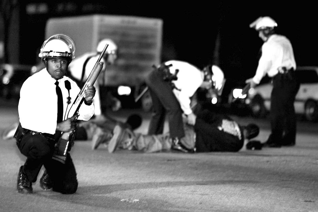 First Place, News Picture Story - Steven M. Herppich / Cincinnati EnquirerCincinnati Police detain two men immediately after an officer was struck by a bullet on his bullet proof vest  while standing near the corner Greenup and Vine Streets late April 11, 2001. The killing of Timothy Thomas, an unarmed African American, by police officer Stephen Roach happened earlier in the week. The shooting lead to one week of protests, riots, and an city imposed curfew leading up to the funeral of this 19-year-old man.