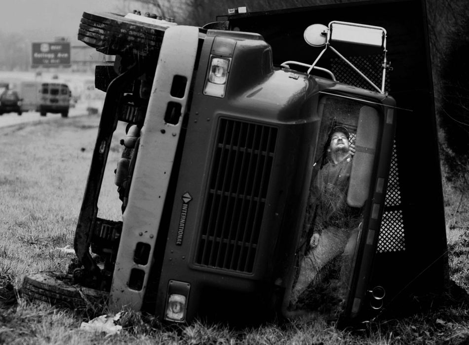 Third Place, Photographer of the Year - Michael E. Keating / Cincinnati EnquirerTony Connelly, a driver for Builder's First Source, prepares to climb from the cab of his overturned flatbed truck just north of the Kellogg Ave. exit of southbound I-275, Feb. 27, 2001. He was slightly injured with scrapes to his head. He reported that he had to slam on his brakes when he encountered a slow moving vehicle and in an effort to avoid a school bus in the adjacent lane. 