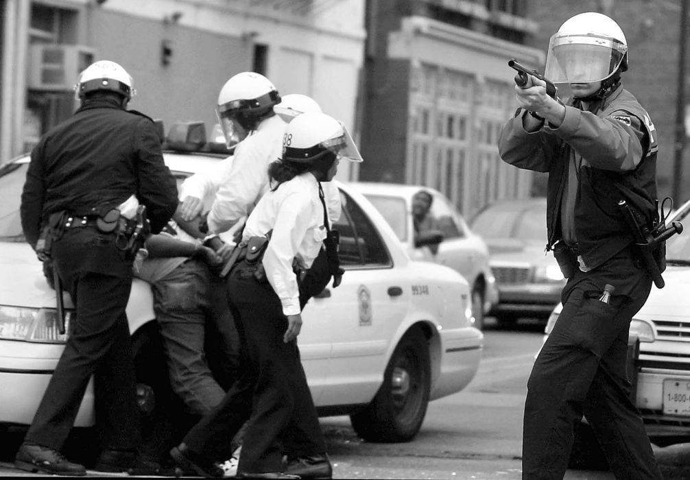 First Place, Team Picture Story -  / Cincinnati EnquirerA man (left) is arrested by Cincinnati Police Officers at the corner of 12th and Vine Streets for refusing to disperse. A police officer (right) fires non-lethal beanbag projectiles into the crowd. 