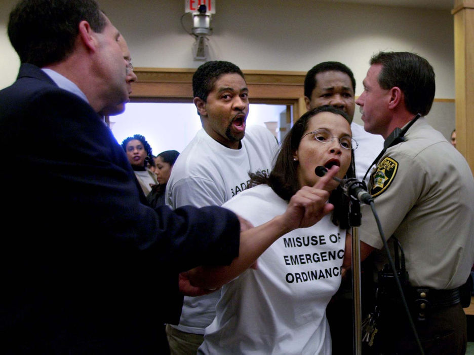 Award of Excellence, General News - Brandi Stafford / The Cincinnati Enquirer Lynn Watts of Evendale yells some last words into the microphone while being arrested by Evendale Police officers as her husband Wyndel Watts attempts to stop them during a city council meeting. Mrs. Watts went over her allotted time limit of one minute and a half to speak and was warned by the mayor then arrested immediately. Mrs. Watts, along with other Evendale residents, were upset with the return of Stephen Roach, a former Cincinnati police officer who killed an unarmed black man last year, onto the police force in Evendale. 