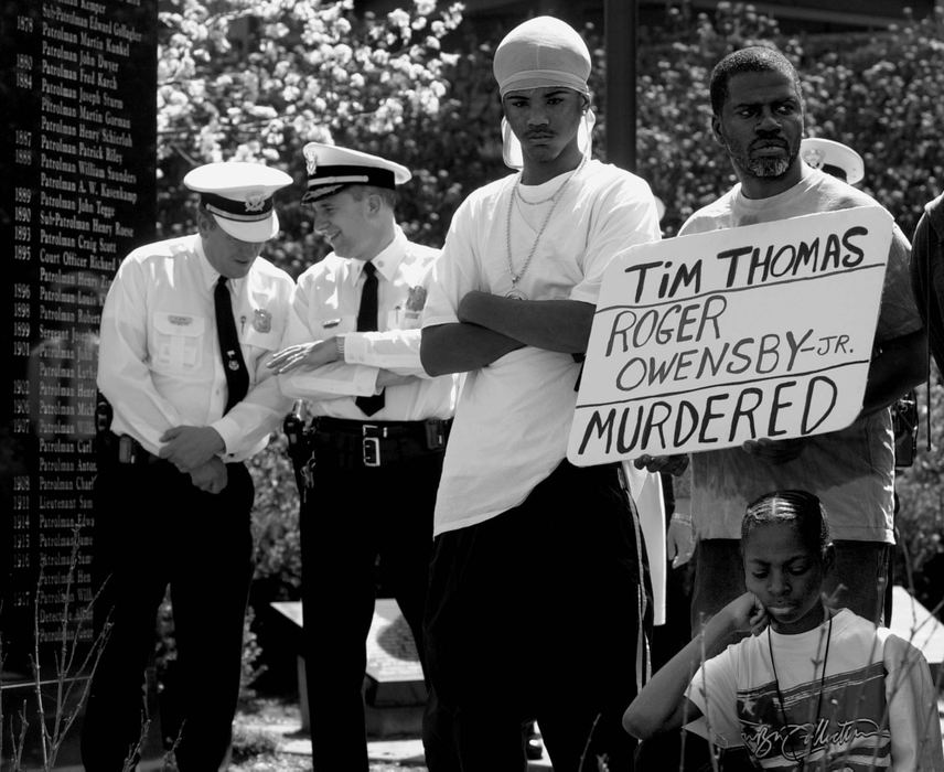 Award of Excellence, General News - Michael E. Keating / Cincinnati EnquirerCincinnati Police officers, accused of abusive behavior against African American males, share a joke in the background as protestors gather at the police memorial to remember Timothy Thomas and Roger Owensby, Jr.. The two were among several black males that died from gunshots and/or alleged abuse while in police custody. 