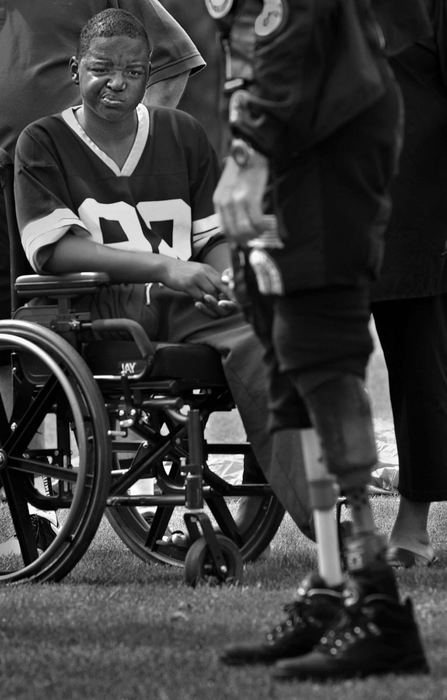 First Place, Photographer of the Year - Ed Suba, Jr. / Akron Beacon JournalLeroy Sutton, no doubt wondering if he will someday be in the same position,  stares at the artificial limbs of Dan Bowman after Bowman parachuted onto the Fox Den golf course in Stow during the Ken Venturi National Amputee and Junior Amputee Golf Tournament. Bowman travels around the country trying to inspire people in Leroy's situation. The 11-year-old Akron boy lost both his legs on the morning of December 7, 2001 after being pulled beneath a train while walking to school with his brother, Tony. 