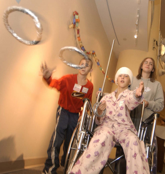 Second Place, Photographer of the Year - John Kuntz / The Plain DealerJennifer Vinkler, 13, (center) of Mentor-on-the-Lake throws rings with her brother Johnny as her older sister Pam mans the wheel chair during a games and crafts party in Rainbows Babies and Childrens Hospital at University Hospital for kids who are staying overnight September 25, 2002.  Jennifer's seizure epicenters were buried in her memory and linguistic portion of her brain and the brain removal surgery was too risky.