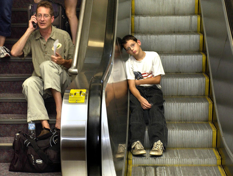 Second Place, Team Picture Story - Chris Stephens / The Plain DealerJeff Bowman talks to his wife in Atlanta while Nathan Klayko,12, takes a rest on a stopped escalator at Cleveland Hopkins Airport International Airport.  Air travel stopped when power went out there.