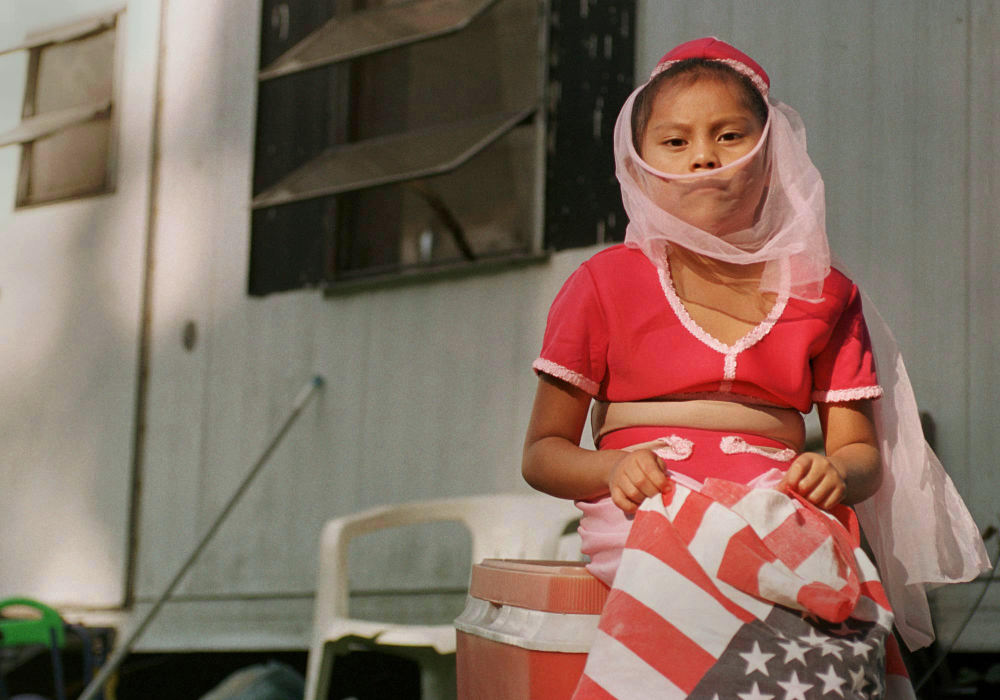 First place, James R. Gordon Ohio Understanding Award - Gary Harwood / Kent State UniversityStill in her genie costume, a migrant child holds an American flag as she sits in the shade by a mobile home in Royer camp. She waits for her turn to participate in activities during a costume party.