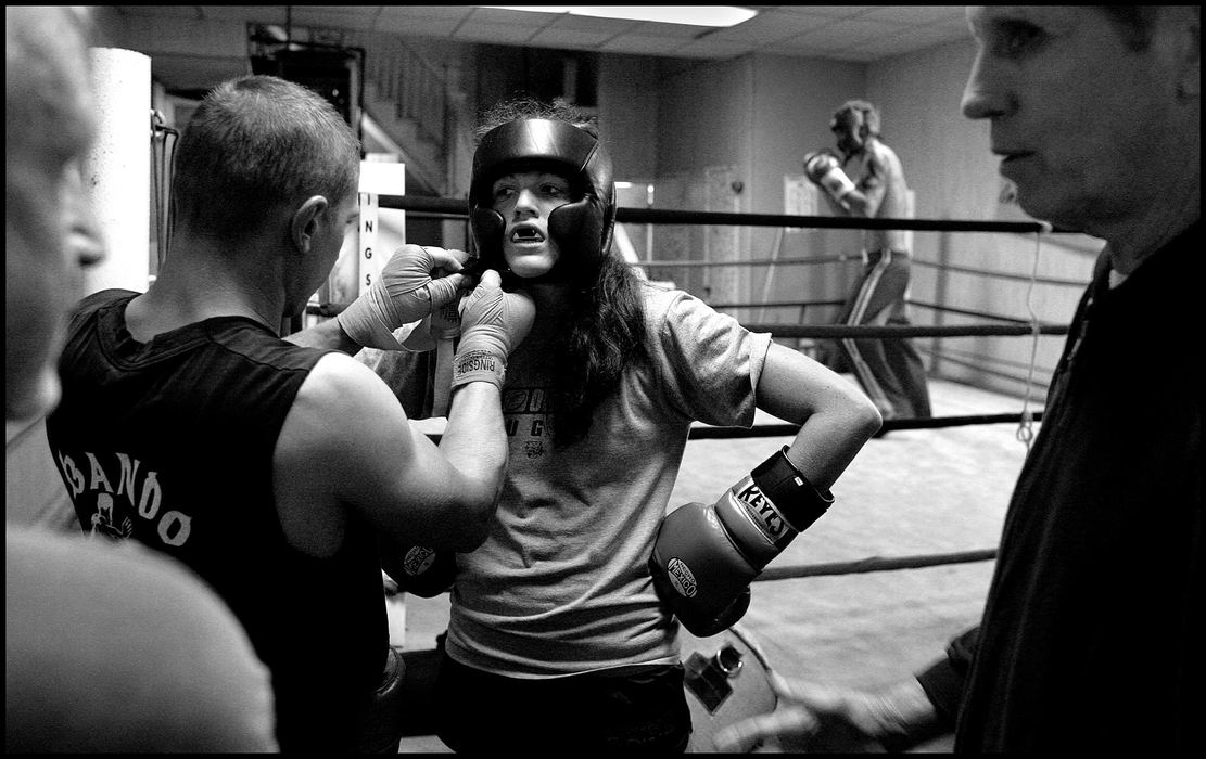 First place, Student Photographer of the Year Award - Katie Falkenberg / Ohio UniversityAs Sam, her coach as well as the gym’s owner, discusses her next organized fight with another trainer, Jessica receives a helping hand putting on her headgear before taking the ring.