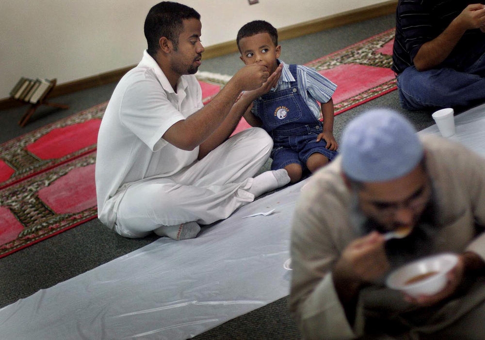 First place, Student Photographer of the Year Award - Katie Falkenberg / Ohio UniversityA father helps feeds his young son during the large gathering to break the fast on the first day of Ramadan, at the Islamic Center in Athens. 