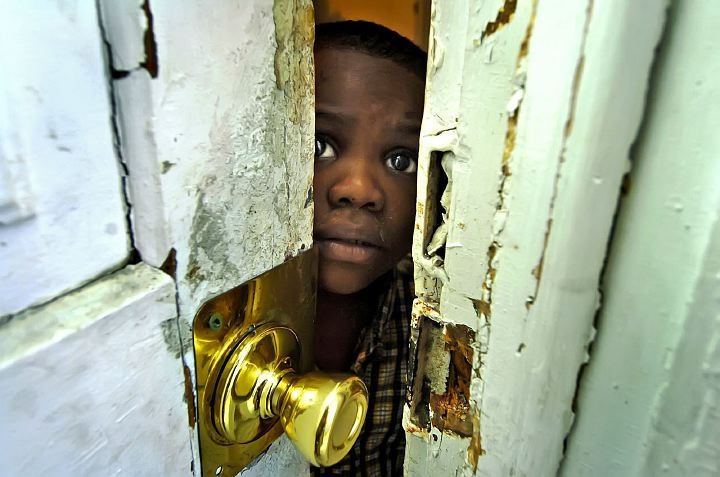 Award of Excellence, Assigned Feature - Glenn Hartong / Cincinnati EnquirerFive year-old Marquise Taylor lives with his family on Dreman Avenue in South Cumminsville. He, his brother, and two sisters all have elevated levels of lead in their bodies. Here, he peers through the front door, which tested positive for lead paint. Lead is released into the environment, often through physical abrasion caused by by the opening and closing of door and windows. Marquise now suffers from behavioral and learning disabilities and will suffer life-long damage.