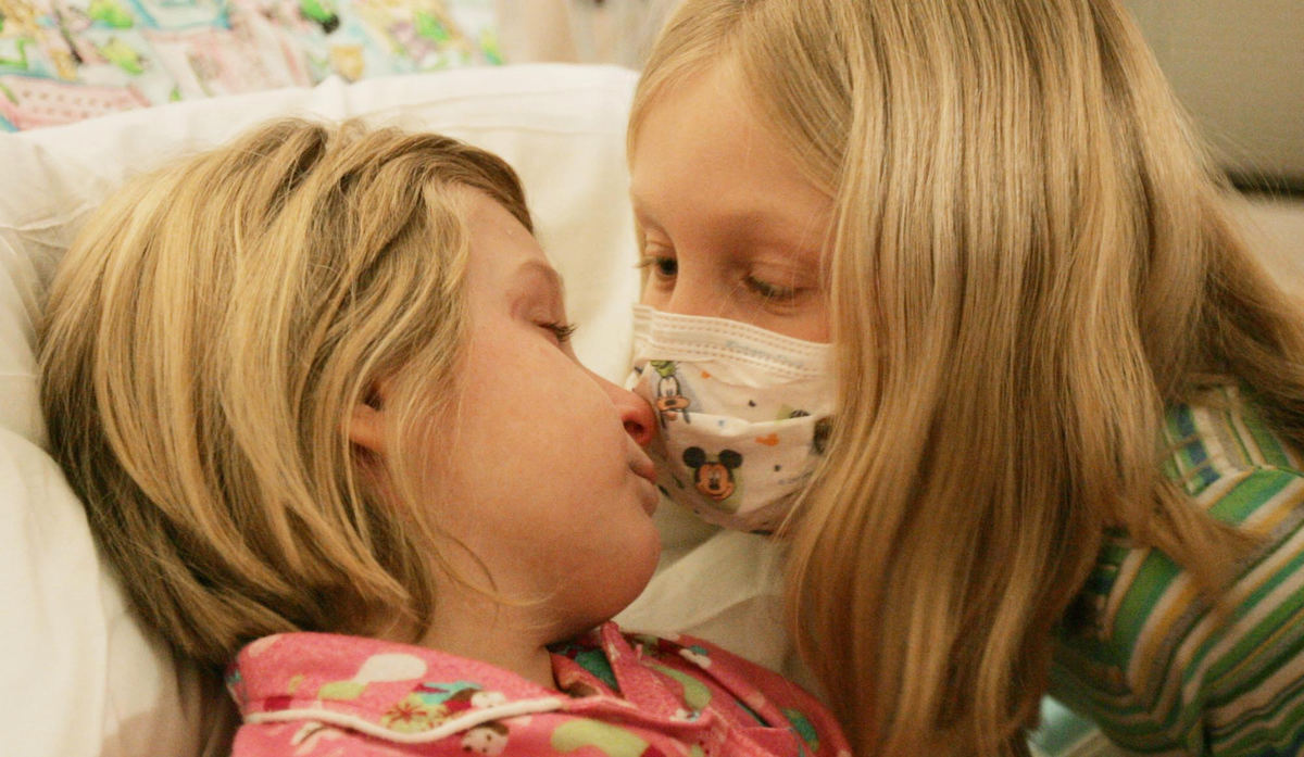 First Place, Feature Picture Story - John Kuntz / The Plain DealerBailey gives her sister Dakota a kiss through her mask cause Bailey had been sick earlier in the week in the 5200 ward at Duke Medical Center January 26, 2006.  Bailey and her father Ken were in for a visit from Olmsted Falls as Dakota goes through the three chemotherapy treatments before the cord blood transfusion.  