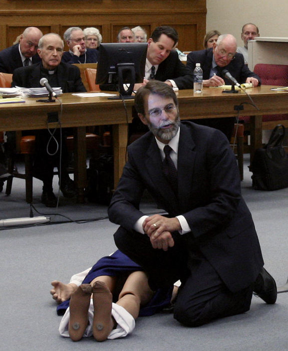 First Place, News Picture Story - Andy Morrison / The BladeLight from a projector illuminates the face of Assistant Lucas County Prosecutor Dean Mandros as he uses a mannequin to illustrate the body of Sister Margaret Ann Pahl while questioning a witness in the murder trial of Rev. Gerald Robinson on April 24, 2006, in Toledo. Robinson, sitting behind at left, a Roman Catholic priest, is accused of killing Sister Pahl in a hospital chapel in 1980. 