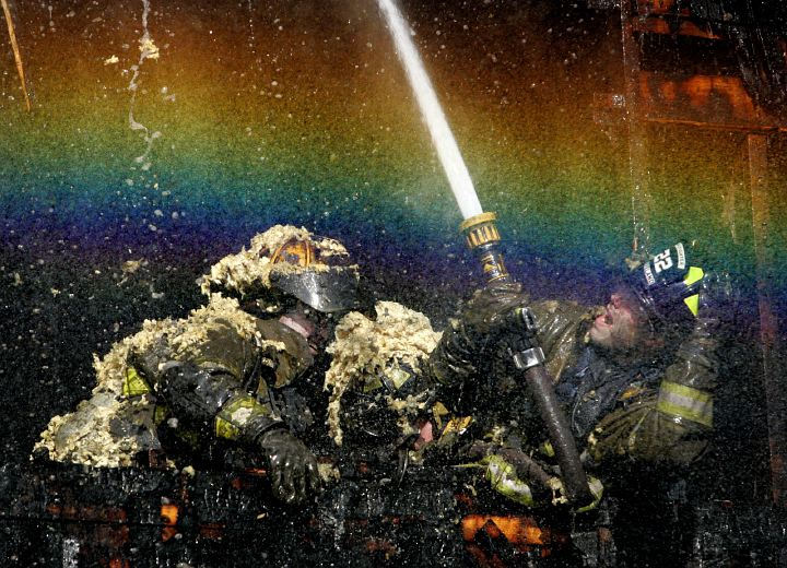 Award of Excellence, Spot News over 100,000 - David I. Andersen / The Plain DealerA rainbow forms in the mist from the water being sprayed by Cleveland firefighters as they battle flames in the peak of the roof of a vacant  house on East 109th Street.  Insulation from the attic covers the firefighters.  No injuries were reported.