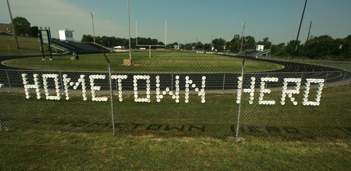 Award of Excellence, News Picture Story - Ken Love / Akron Beacon JournalA message to the family of U.S. Army Cpl. Zachary A. Grass, 22, made of foam cups is on a fence at  Brideweser Stadium at Fairless High School in Navarre. Fairless High School graduate, Zachary A. Grass was killed in a roadside bombing in Iraq. Hundreds from this rural community, attended the funeral and graveside services to honor this fallen soldier.