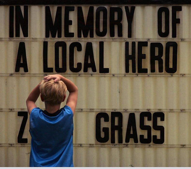 Award of Excellence, News Picture Story - Ken Love / Akron Beacon JournalAlex Jamison, 8, pauses in front of a sign along the funeral procession of U.S. Army Cpl. Zachary A. Grass, 22, in Sugarcreek.  