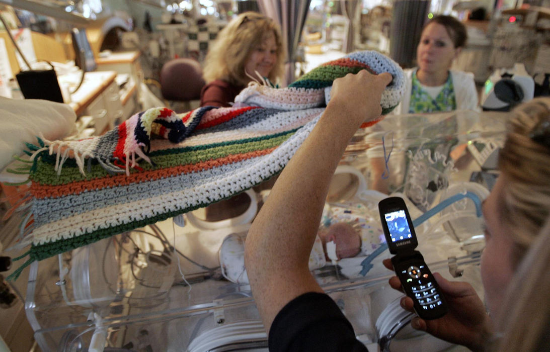 Second Place, James R. Gordon Ohio Understanding Award - Chris Russell / The Columbus DispatchBeth lifts a blanket that shields Riley's eyes from  light and takes a photograph with a camera phone during a visit to Children's Hospital with her mother. They are still months away from being able to touch or hold Riley. 