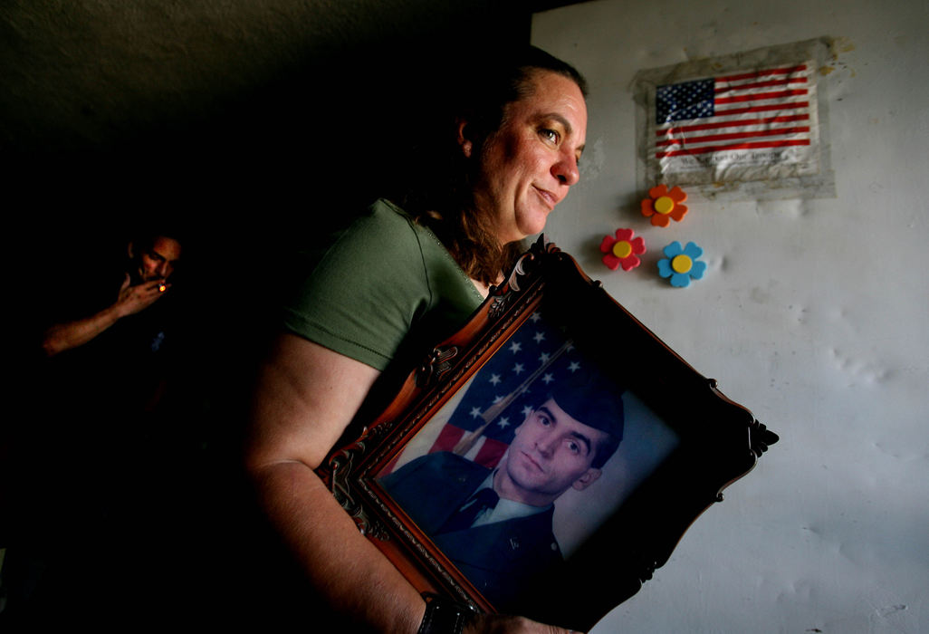 Second Place, Photographer of the Year - Lisa DeJong / The Plain Dealer "I miss him," Roxane Dowdy says as she holds a picture of her brother First Sgt. Robert Dowdy, 38, at her front door of her home. She misses his wry sense of humor.  "Nothing is ever the same. It  changes everything."  Robert Dowdy was killed in Iraq on March 23, 2003, during the notorious Jessica Lynch ambush. The wrinkled, Scotch-taped, paper "We Support Our Troops" American Flag has been on her front door since the war started. (In background smoking on left, is Roxane's brother Jim Dowdy, 40.)