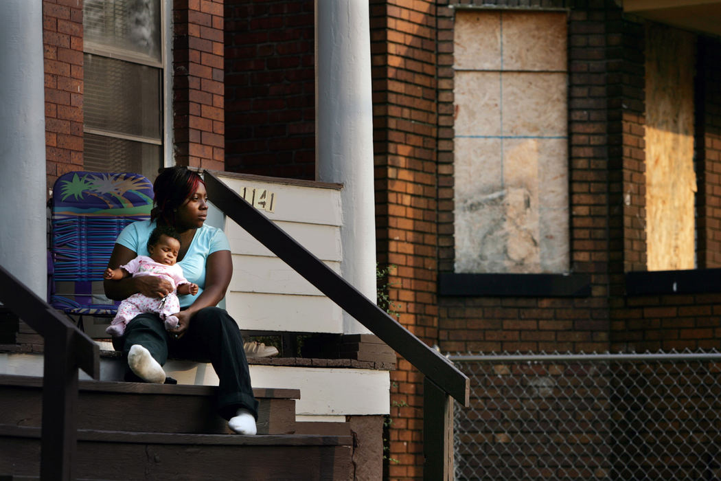 Third Place, Photographer of the Year - Gus Chan / The Plain DealerEast 71St., in Cleveland, typifies what is happening to our neighborhoods.  Drug dealing, foreclosed homes, an aging population compounded by an aging housing stock has put neighborhoods in crisis. Desiree Smith holds her two-month-old daughter Brionna Crute as she watches from her porch the goings on E. 71 St.   Smith moved in with her family three weeks ago.  Her mother lives in the adjoining unit.  The two apartments are next to a complex of abandoned units.