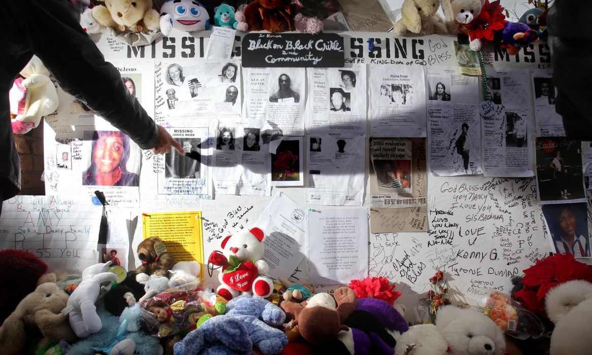 Second Place, News Picture Story - John Kuntz / The Plain DealerA woman points to a missing persons poster of her friend, Janice Webb who was one of the eleven identified at the home of alleged mass murderer Anthony Sowell, on a memorial wall November 10, 2009 created for loved ones missing in the Cleveland area located across the street from Sowell's home on Imperial Avenue.   The missing persons board that was fastened to a fence has grown to a board of unsolved murders in Cleveland with signs, candles and stuffed animals to honor the dead. 