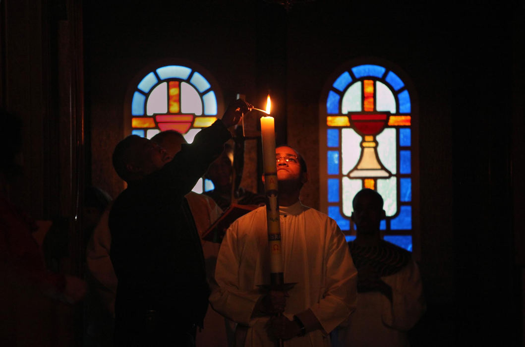First Place, News Picture Story - Gus Chan / The Plain DealerThomas Sutton-Lovett, a seminarian who grew up in St. Adalbert Church, holds the Easter candle as it is lit before the Holy Saturday Vigil.