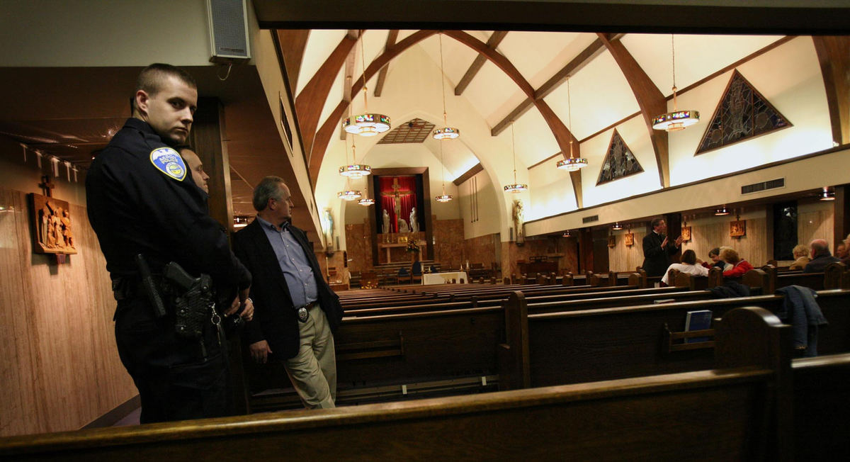 First Place, James R. Gordon Ohio Understanding Award - Gus Chan / The Plain DealerAkron police watch over protesters inside St. John the Baptist Church as Bishop Richard Lennon addresses the small group.  Bishop Lennon was at the Akron church to preside over the final mass.