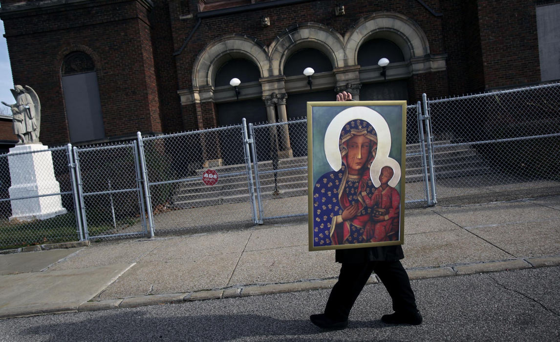 First Place, James R. Gordon Ohio Understanding Award - Gus Chan / The Plain DealerKristina Moreno carries off a portrait of the Black Madonna after a  morning prayer service outside the closed St. Casimir Church.  About a hundred people turned out for the service a month after the church closed it's doors. 