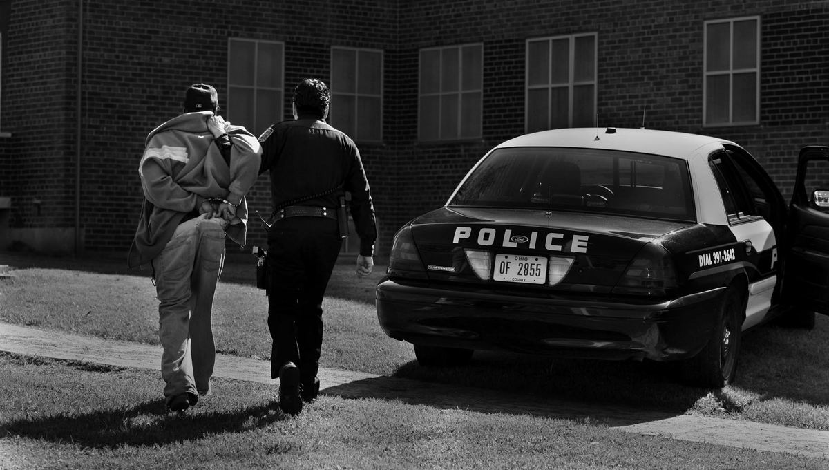 Second Place, Photographer of the Year Large Market - Gus Chan / The Plain DealerCuyahoga Metro Housing Authority police officer Clint Ovalle leads a suspect to his police cruiser to be detained while searching for drugs at CMHA's Lakeview Terrace property.