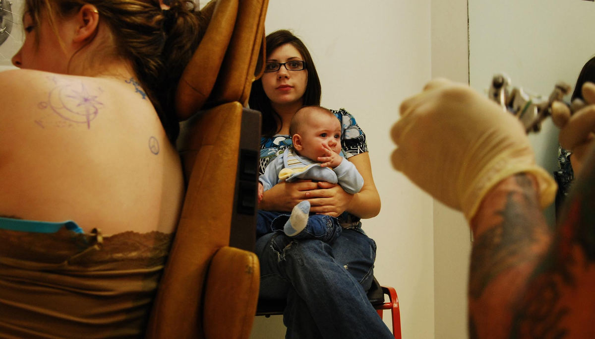 Third Place, Photographer of the Year Small Market - Tessa Bargainnier / Kent State UniversityKaila Lipstreu, 16 from Burton, waits to get a tattoo at Mike Ink Tattoo Studio in Mantua. Her 5-month-old son, Anthony Zohos, sits on 19-year-old Rachel DeSalvo’s lap waiting for Mike Krestan to tattoo a star and moon on Lipstreu’s back. 