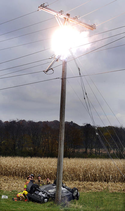 Second Place, Spot News (under 100,000) - Bill Lackey / Springfield News-SunUrbana firefighters, attempting to rescue the driver of an overturned car that struck a utility pole, look up at the arcing wires that are exploding above them, Oct. 28 2009 along Ohio 68 in Champaign County. Part of the pole broke when the car struck it causing the charged wires to arc and catch fire.  