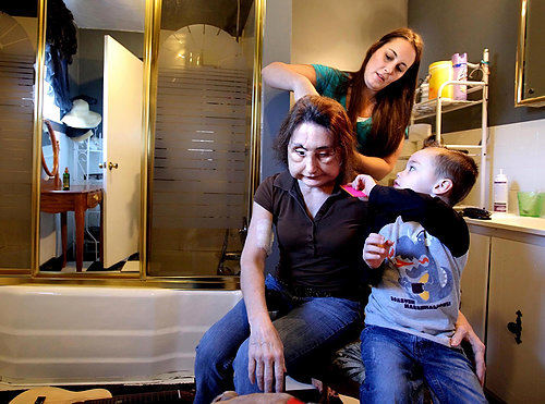 Second Place, Feature Picture Story - Lisa DeJong / The Plain DealerConnie Culp's daughter, Alicia, uses a straightening iron on her mother's hair while Alicia's son, Maddox, 3, helps out with a comb. Alicia says the texture of Connie's hair has changed because of her surgeries. Tom Culp, her common-law husband, shot her in the face in 2004 and left her with no right eye or nose, no lower eyelids, upper lip or top teeth.  After doctors removed scar tissue, bone grafts, and metal from her previous surgeries, Culp received 80 percent of the face and underlying tissue of an organ donor.