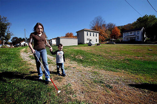 Second Place, Feature Picture Story - Lisa DeJong / The Plain DealerConnie, who is legally blind, uses her white cane while walking near her home in rural southern Ohio with her 3-year-old grandson, Maddox. The shooting that destroyed her face stole most of her vision, too, making it impossible for her to read, drive or work. "If I run into walls, I'm good at bouncing, " she says, humor in tact as always. Neighbors are used to Connie on the winding roads and slow down through her street. 