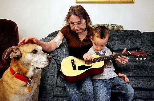 Second Place, Feature Picture Story - Lisa DeJong / Connie helps Maddox with his guitar who loves all things music. Baby Girl, her dog, is never very far away.