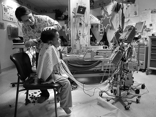 Third Place, Feature picture story - Michael E. Keating / MIchael E. KeatingA nures gives Manny a much needed haircut, a scene not often played out in a hospital room. Manny Evans, 7, has lived five of his seven years as a resident of Cincinnati Children's Hospital Medical Center.  Diagnosed with neurofibromatosis the genetic disorder that forms tumors that surround nerves, Manny  requires medical and nursing care beyond what can be provided in a residential environment.  His mother chooses to let him live at the hospital instead of a residential center or nursing home.  Manny recently began his schooling at Roselawn Condon School and a school bus picks him up each day in front of the hospital.  A fleet of nurses, personal attendants and caregivers provide the love and care, emotionally and physically, often the responsibility of a parent.  