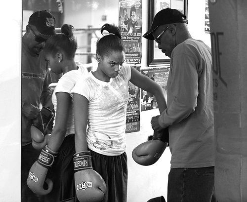 Second Place, Sports Picture Story - Carrie Cochran / Cincinnati EnquirerRay Robinson, 64, of Millvale, helps his 13-year-old daughter, Raynesha, put on her boxing gloves at the Millvale Recreation Center before practice begins. Ray is a single father raising his two children."She's gonna hang with me. She's not going to be hanging with her friends," he said. Raynesha's had been failing her classes and Ray believes it's because she had been hanging around kids from the neighborhood. He raises Raynesha and Ray Ray, 10, in a small apartment in a government-subsidized housing project, where gun violence and teen pregnancy are commonplace.