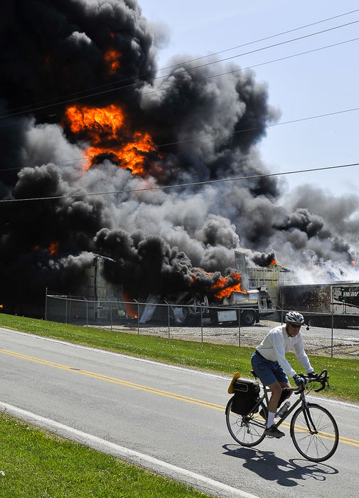 First place, Photographer of the Year - Small Market - Bill Lackey / Springfield News-SunA bicyclist rides past a fire at the RD Holder Oil Co. in rural Clark County, Ohio Thursday, April 19 2012. The fire, which started when a tanker truck caught fire near the companies warehouse, quickly engulfed the entire business. Fire fighters battled the blaze for more than six hours.