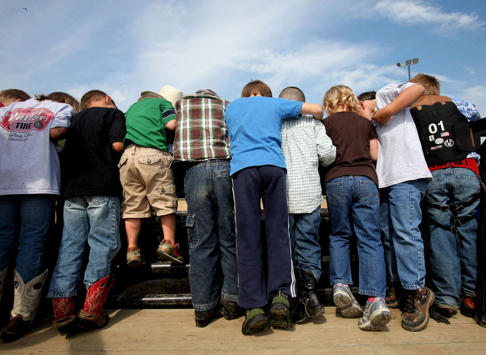 Second Place, Photographer of the Year - Large Market - Lisa DeJong / The Plain DealerBuckaroos, ages 5-9, stretch to get a better look  into a bucking chute as instructors show them a Suffolk sheep that they will be riding. The brave cowboys and cowgirls are taming the flying fleece at the Mutton Bustin' School. The Mutton Bustin' School, staffed by professional bull riders, teaches buckaroos ages 5-9 years old how to safely hold onto the sheep's pelt as they ride across the dusty ring. The simple premise is to ride until you fall off. 