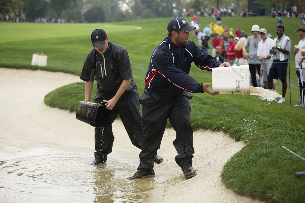 Third Place, Team Picture Story - Lisa Marie Miller / The Columbus DispatchFrom left to right Ben Dewan and Travis Russell (cq) use buckets to bail out water on the bunker of the 13th hole during the second round of the Presidents Cup at Muirfield Village Golf Club in Dublin, Ohio on Saturday, October 5, 2013. The men are both interns with the Maintenance Crew and it was the first summer they worked at Muirfield.  The men were trying to get the water out of the bunker just after play was delayed to rain damage on the course. 