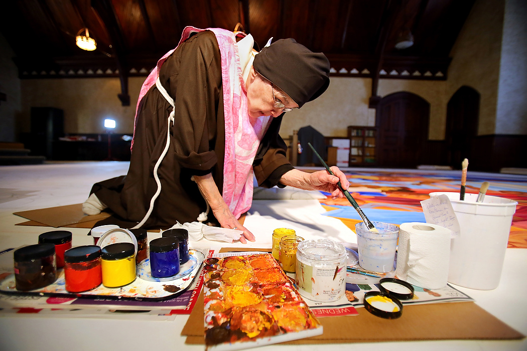 Award of Excellence, Feature Picture Story - Lisa DeJong / The Plain DealerA pink smock with kittens on it protects her vestments from the acrylic paint. Mother Mary Thomas, 81, spends hours on her knees painting a mural titled "Our Lady of the Blessed Sacrament and the Communion of Saints" inside the Adoration Monastery where she has lived for 55 years.  No more than five feet tall, Mother Thomas is a member of the Poor Clares of Perpetual Adoration, a silent cloistered order tracing its origins to the early 13th century. These days, she toils cheerfully on a mural many times her size. Currently, Mother Thomas, 81, spends hours on her knees painting a 30 x16-foot mural that she hopes to present to the pope when he arrives in Philadelphia in September.  "Art is chiefly a prayer for me, an expression of my love for God and His people," she said. Mother Mary Thomas has painted in vivid colors for over 60 years, influenced by studying mural painting in Mexico in her early 20s. A teacher encouraged her to go to the Chicago Institute of Art because, she was told, her work already reflected the influence of Diego Rivera, the famed Mexican muralist. Later, she would work with David Alfaro Siqueiros, a muralist in Mexico. After World War I, the Mexican Muralism style evolved with the intent of creating public art as visual narrative, especially as a means of social commentary and historical perspective.  In 1958, at the age of 25, she went to Rome to further study and paint. During an Easter prayer vigil at St. Peter's Basilica, she said, she was overcome with an intense sense of joy and knew then that joining a religious order was her vocation.  "If you told me then that I would end up in a cloistered order of nuns, I would not have believed it," she said. 