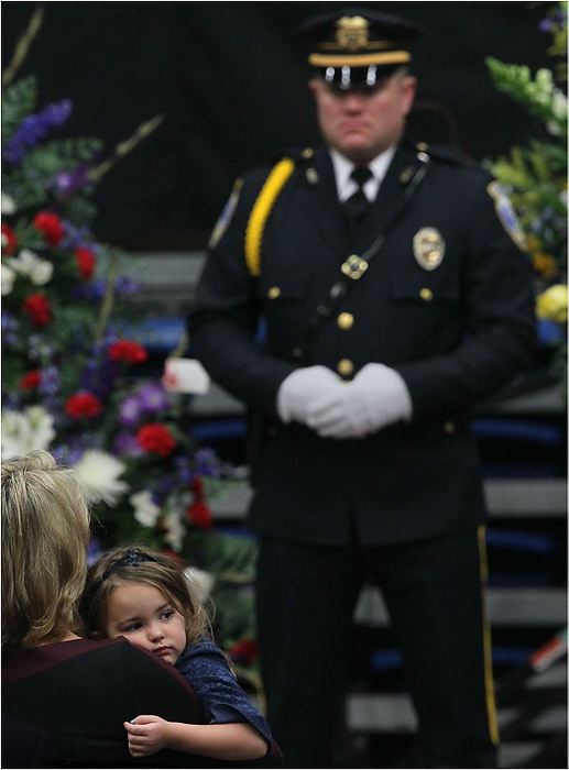 Third Place, News Picture Story - Ed Suba Jr. / Akron Beacon JournalCharlee Ayn Winebrenner (center), the daughter of Akron Police Officer Justin Winebrenner, is held by a family friend during the memorial service for her father at the James A. Rhodes Arena in Akron.