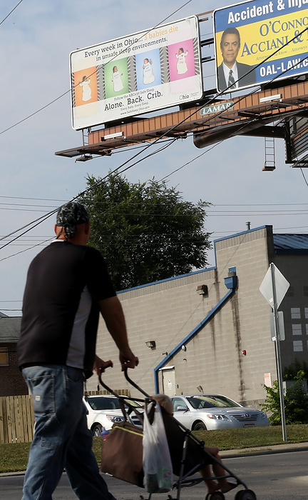 Second Place, James R. Gordon Ohio Understanding Award - Brooke LaValley / The Columbus DispatchA man pushes a stroller while he walks past a billboard advertising the Columbus Health Department's "ABC's of Safe Sleep" campaign on Sullivant Ave. in Columbus, Ohio on August 19, 2014. The "ABC's" of Safe Sleep stand for the words alone, back and crib- asking that parents place infants in their cribs alone and on their backs for bedtime to prevent complications. 