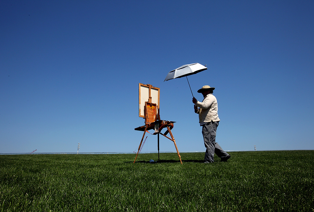 Second Place, Photographer of the Year - Large Market - Lisa DeJong / The Plain DealerEd Schmitt, 56 takes his umbrella down that shaded his yet-to-be-named masterpiece on the huge grassy area of Mall C, on top of the Cleveland Convention Center. Schmitt has been working on this oil painting, which includes the skyline of downtown Cleveland and Santa Maria coming out of the clouds, on and off for years. It will take him years to finish it, he said. The inspiration to start painting again "en plein air" was his recent retirement from the Cudell Fine Arts Center. 