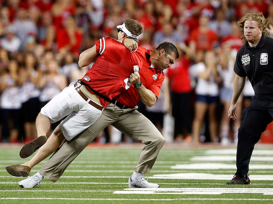 Award of Excellence, Sports Feature - Adam Cairns / The Columbus DispatchAs security closes in, Ohio State strength and conditioning coach Anthony Schlegel tackles Anthony Wunder, a 21-year-old mechanical-engineering student at OSU, after he ran onto the field during the second quarter of a game against the Cincinnati Bearcats at Ohio Stadium in Columbus. Wunder was eventually arrested and charged with criminal trespassing.