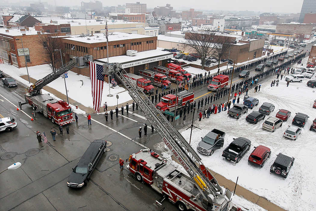 First Place, Team Picture Story  - Jetta Fraser / The (Toledo) Blade A limousine follows the Toledo Fire Department truck carrying the flag-draped coffin of firefighter Stephen Machcinski past TFD Station No. 5 during his funeral procession.  He worked out of station 5.