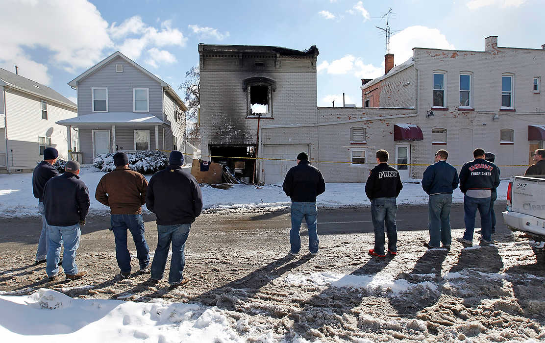 First Place, Team Picture Story  - Dave Zapotosky / The (Toledo) BladeFirefighters from the Sandusky and Perkins Township fire departments view the apartment building in North Toledo  where two Toledo firefighters were killed while battling a fire on Sunday.  Firefighters Stephen A. Machcinski and James A. Dickman were killed. Dickman was a Perkins Township firefighter before joining the Toledo department. The firefighters place a Perkins Township Fire Department t-shirt and gloves on a board propped against the wall of the burned building.  