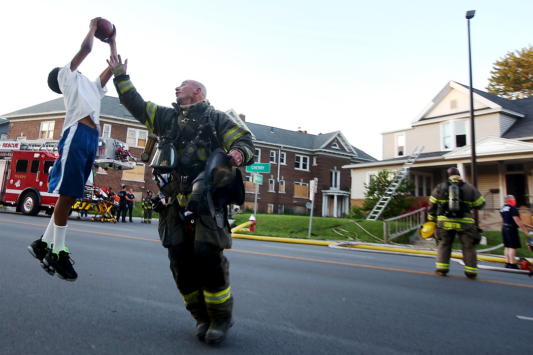 Third Place, Spot News - Katie Rausch / The BladeLt. Pete Traver can't cover Tabari Triplett, 11, as he plays football with some friends from the neighborhood after Toledo firefighters had extinguished a blaze at a house on Cherry Street in Toledo. 
