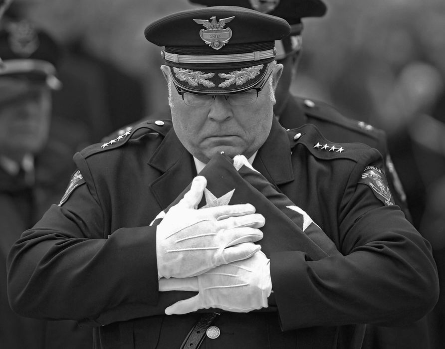 First Place, News Picture Story - Kyle Robertson / The Columbus Dispatch, "Westerville"Westerville Police Chief Joseph Morbitzer walks slowly to presents the American flag that was over the casket of Westerville officer Morelli to his wife Linda and family after funeral services at St. Paul Catholic Church in Westerville on February 16, 2018. 