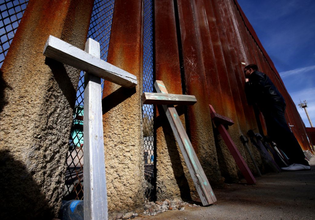 Second Place, News Picture Story - Lisa DeJong / The Plain Dealer, “Border Wall”Wood painted crosses left for loved ones are leaned against the border wall in Nogales, Sonora, Mexico. Bryan Martinez Miranda, 24, who lives in Nogales, Sonora, Mexico, leans in close from the Mexican side to speak with his mother Norma Alicia Miranda Leyva, 53, through the border wall. Bryan is studying renewable energy in Mexico. Norma lives in the United States directly across the street from this spot in the turquoise house in the background on West International Street. Leyva wanted to live as close as possible to the border. When her arthritis flares up and she cannot walk down the stairs from her second-floor, one-room apartment, she steps out onto her balcony and waves to her son looking through the border wall. "It's been four years since I was able to hug any of my sons," she said through a translator. She said she became upset when she heard a rumor that Trump was planning to replace the current wall with a solid, metal one. "That would have been terrible," she said. "It's hard enough now, but at least we can touch and see one another. I don't know if I could stand being unable to do the little we can."