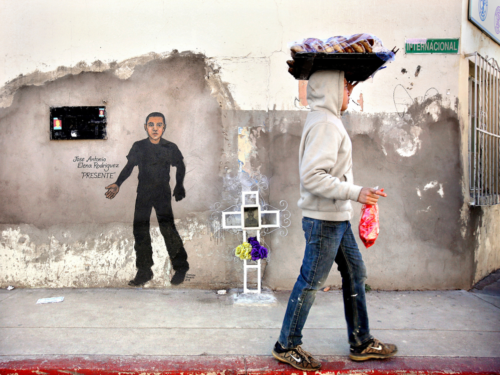 Second Place, Photographer of the Year - Large Market - Lisa DeJong / The Plain DealerA young man carrying bread walks by a shrine in honor of Jose Antonio Elena Rodriguez, the spot where the 16-year-old boy was shot and killed in October 2012 by a U.S. Border Patrol agent on the corner of Calle Internacional and Ingenieros streets directly across from the border wall on the Nogales, Sonora, Mexico side. Bullet holes can still be seen in the wall on the upper right hand side. The boy was shot eight times in the back and twice in the head by American Border Patrol agent Lonnie Swartz in 2012 in response to rock throwers. The chief of internal affairs for Customs and Border Protection was quoted saying it was the most egregious shooting he had ever seen. American juries acquitted Swartz of murder and involuntary manslaughter charges in two trials.