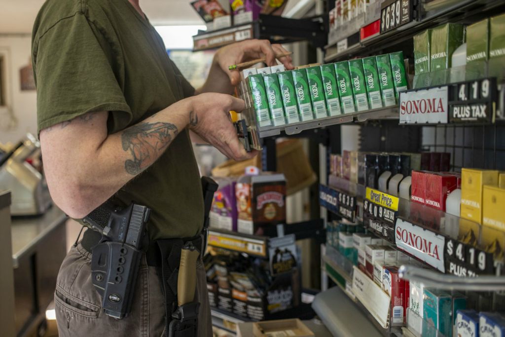 Third Place, Chuck Scott Student Photographer of the Year - Lauren Santucci / Ohio UniversityCharles Bobo wears a Glock, three magazines and a knife on a tactical belt while he works the register at the gas station in the village. With no local law enforcement, residents feel a responsibility to protect their property, family, and the rest of the community. 