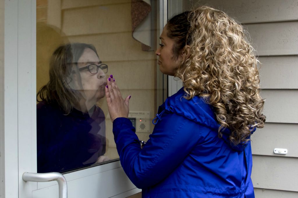 First Place, George S. Smallsreed Jr. Photographer of the Year - Small Market - Jessica Phelps / Newark AdvocateJoAnn Poulton presses her hand up to glass door to say goodbye to her mom, Kathy Poulton who leans in to kiss her hand on March 17, 2020. Kathy is a resident at the Inn at Chapel Grove, a senior living facility in Heath and is living with dementia. In some ways, JoAnn thinks her mom having dementia is easier for her in this time, so she doesn't get scared, but also knows her mom doesn't understand why she can't enter the building and give a hug. "Its hard," she said. "Every week we lose a little more of her."