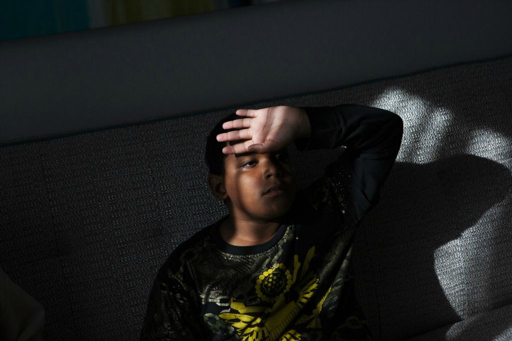 Award of Excellence, Portrait Personality - Madeleine Hordinski / Ohio University, “PJ Bolden”PJ Bolden, 8, watches TV in his hotel room in Cincinnati on March 23, 2020. PJ’s family has been staying in the Cincinnati hotel for a couple weeks. He and his family have been homeless since the end of February, and were forced to move into the hotel after the shelter they were staying in shut down because of the pandemic. Luckily, the shelter managed to find funding to help families. Thus, PJ is able to stay with his family in a moderately isolated space during the pandemic, but the isolation brings a lot of tension. He has to share one bedroom with the other three members of his family until his mom is able to find an apartment for them to move into.